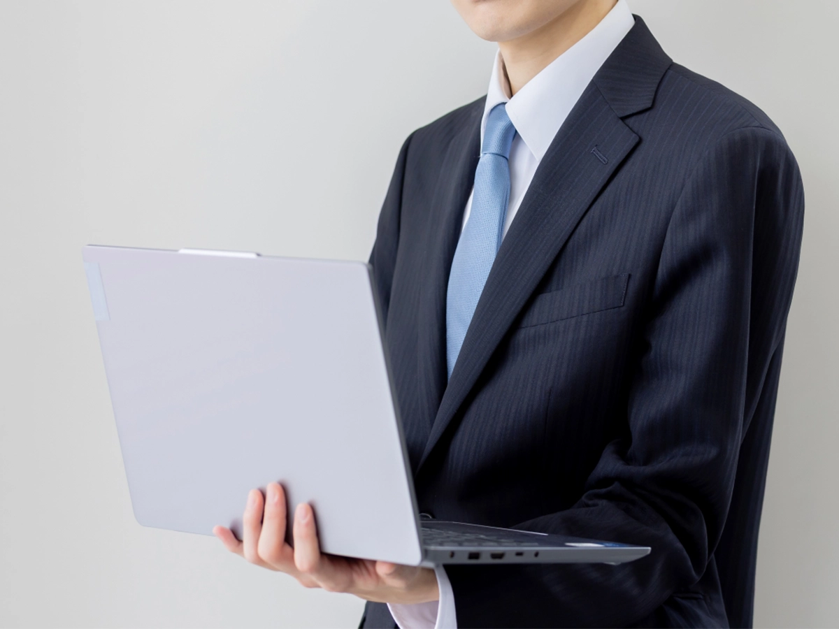 ノートパソコンを持つ男性が業績データを確認している様子。数字で経営判断を行う支援イメージ